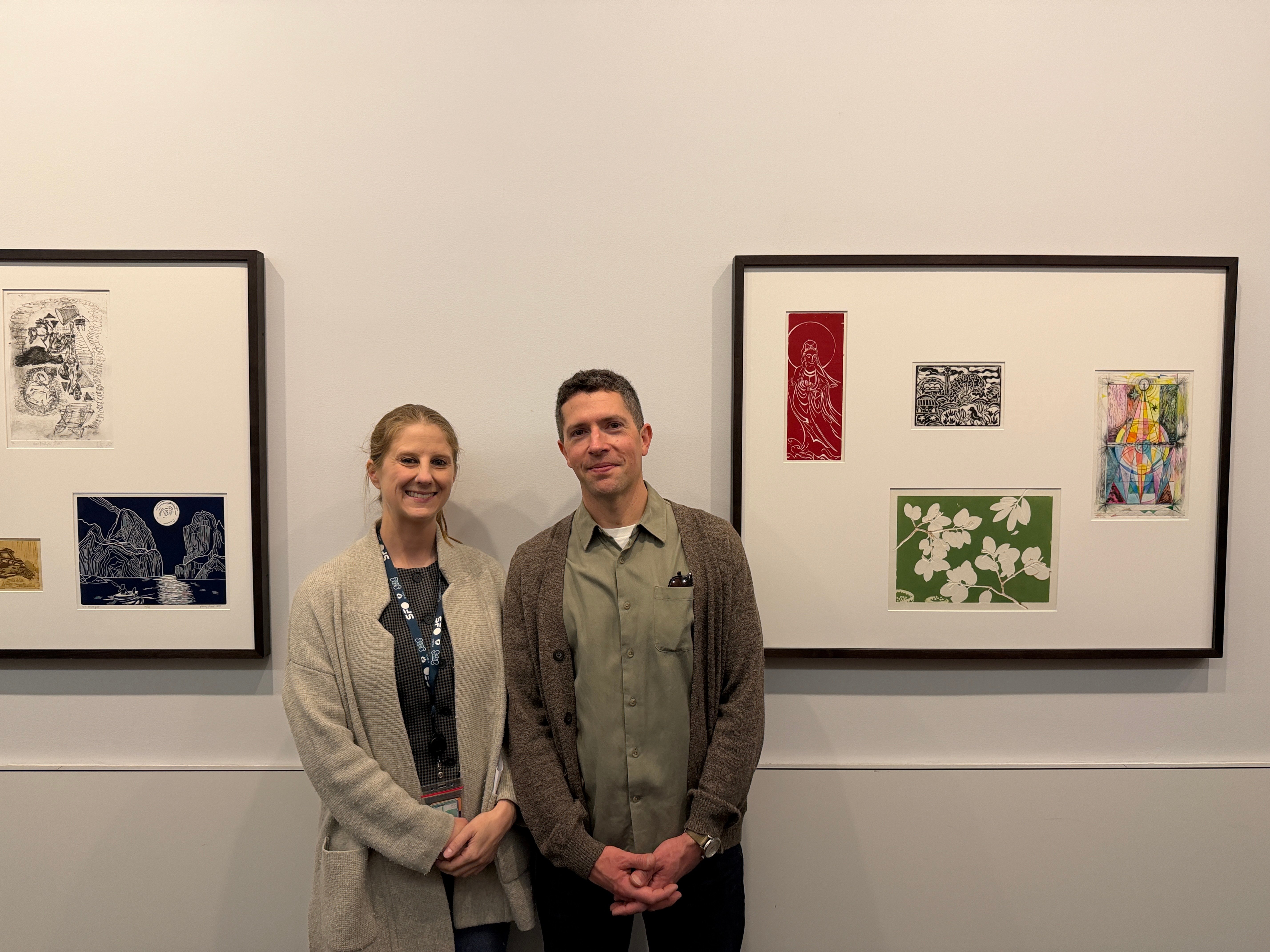 A smiling woman next to a smiling man stand in between two picture frames. They are Allie Haeusslein, SFO Museum Curator of Photography and Student Art, and Alex Echevarria, Laney College art professor. They are the co-curators of the SFO exhibit "Shared Impressions" featuring Laney student art.