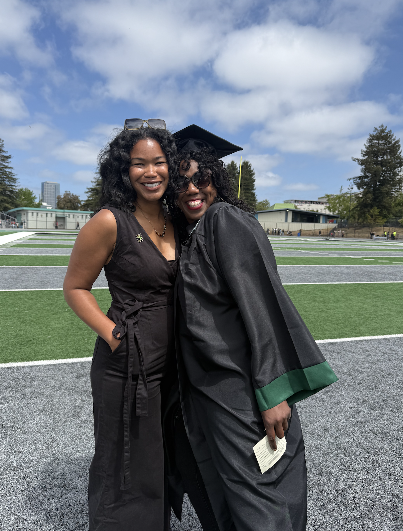 Two women smiling at Laney College on graduation day in 2025. They are Nik Howell (in a black dress) and Rikki Gates (in a black and green graduation gown).