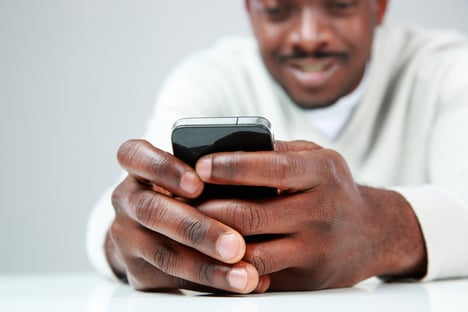 African man sitting at the table and using smartphone. Focus on smartphone