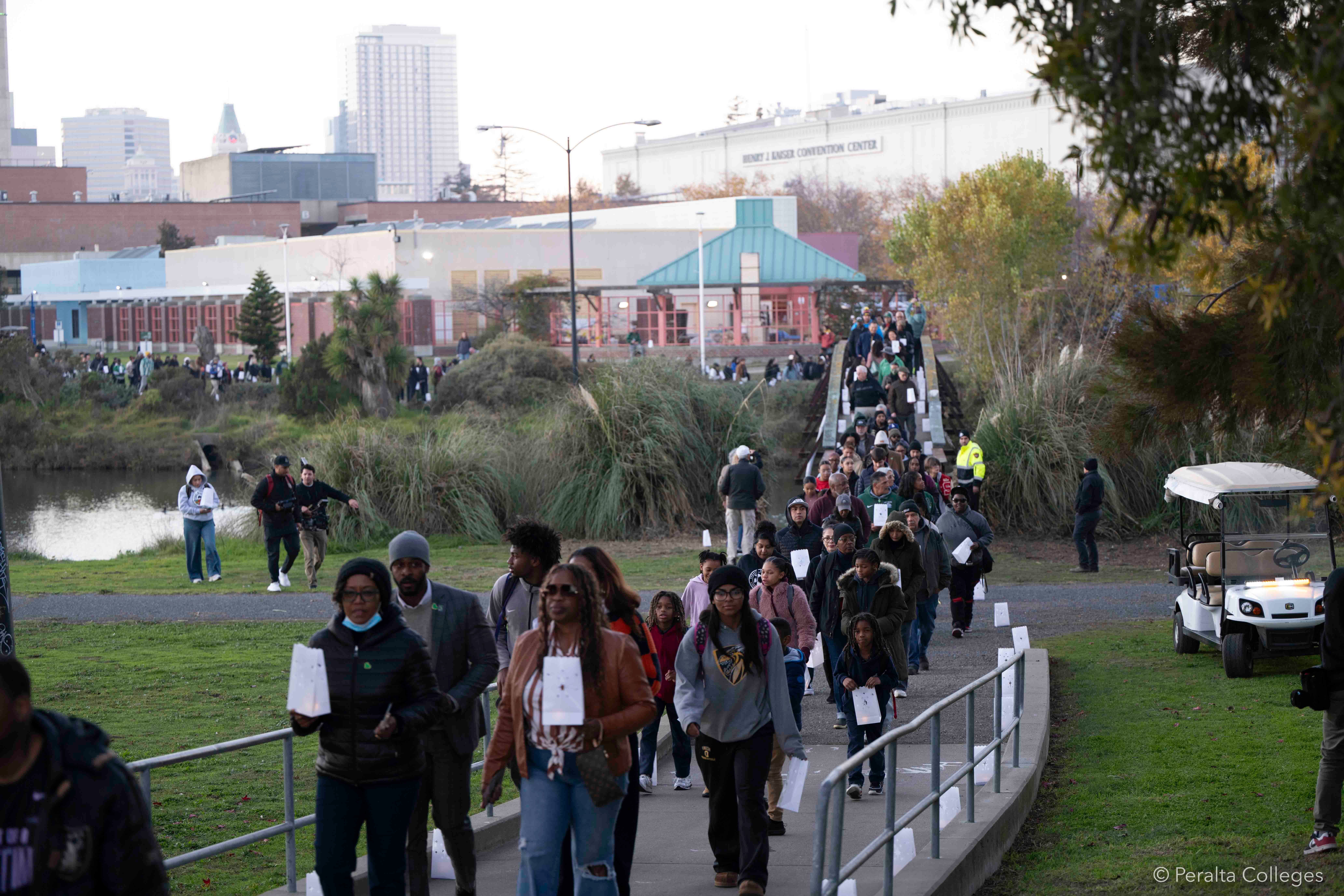 People with luminaria lanterns walking on a bridge over the Lake Merritt estuary between the Laney College main campus and the Laney football field.
